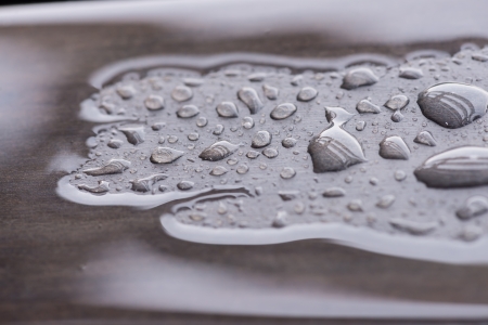 Puddle of rain water and raindrops pattern on wooden table  Reflections of beams in raindrops and woon grain can be seen through the water  の写真素材