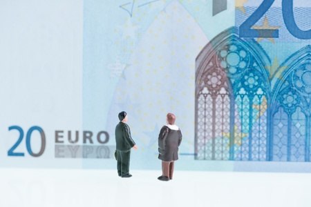 Miniature men looking at the twenty Euro banknote background with the feature of Gothic architectural styleの写真素材