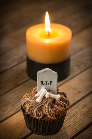Halloween cupcake and candle on a rustic wooden table with dark vignetting effectの写真素材