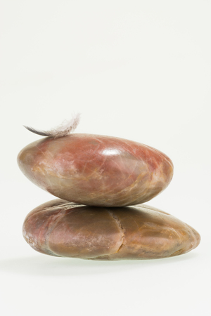 Small down feather balancing on red river stones の写真素材