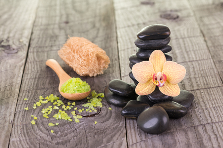 Yellow orchid, bath salt, loofa and black stones on weathered deckの写真素材