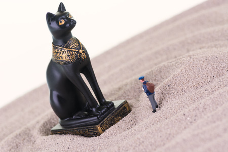 Miniature tourist with the Egyptian guardian Bastet statue on sandの写真素材