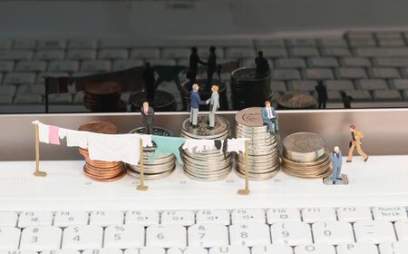 Money laundering concept with miniature people and coins on top of a notebook