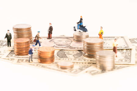 Miniature people on paper currency and coins over white backgroundの写真素材