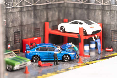 Miniature mechanic checking on the engine while a technician is doing a diagnostic on his laptop at the workshopの写真素材
