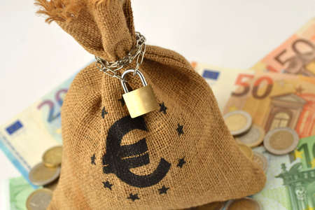 Money bag with padlock and chain over euro banknotes and coins - Saving money and financial security conceptの写真素材