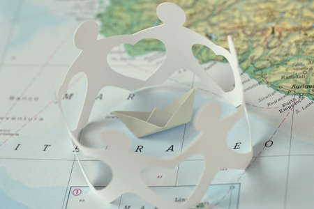 Paper boat and paper people in a circle holding hands on a map - Immigration and solidarity conceptの写真素材