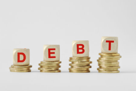 The word debt written with wood blocks on top of coins piles - Debt increase conceptの写真素材