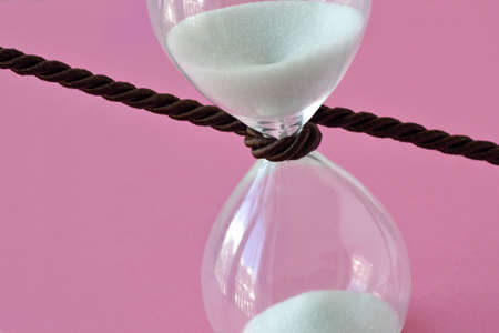 Close-up of hourglass with a cord around it on pink background - Stop the time conceptの写真素材