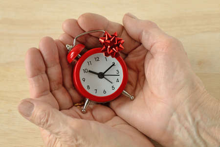 Woman hands holding red alarm clock with gift bow - The gift of time concept; time for gift giving...