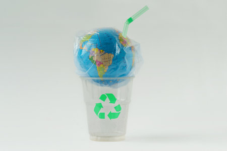 Earth globe in a plastic bag with straw on plastic glass with recycling symbol - Concept of ecology and stop plastic pollutionの写真素材