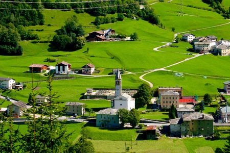 View from Bernina Express, Alpine village with a church in the middle surrounded by green grass meadows の写真素材