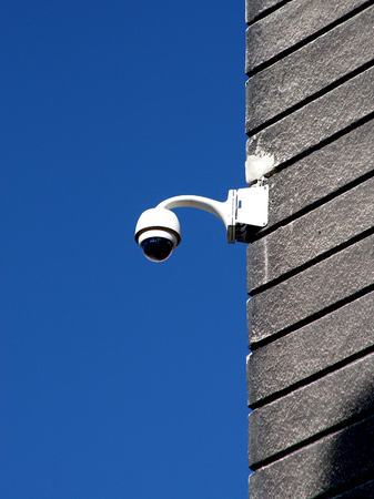 Security camera on plaster covered wall against deep blue 