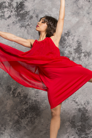 AfricanAmerican female dancer in a red dress on releve in a studio session with a grey mottled background. Vertical image.の写真素材
