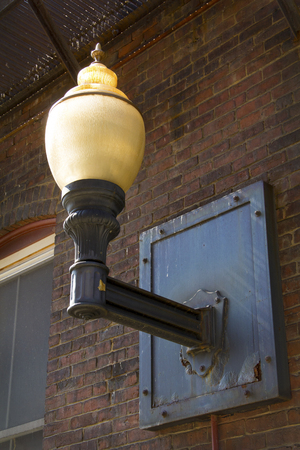 Vintage light fixture, with yellowing glass globe and right angle iron support, on brick wall in alley, downtown Keene, New Hampshire.の写真素材
