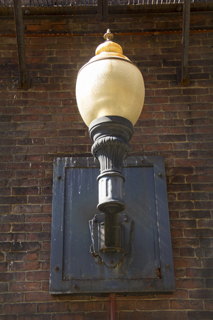 Vintage outdoor light, with yellowing, opalescent glass globe, on brick wall in alley, downtown Keene, New Hampshire.の写真素材