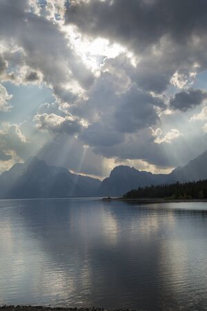 Dramatic dark clouds with sun rays over Jackson Lake, Jackson Hole, Wyoming, vertical.の写真素材