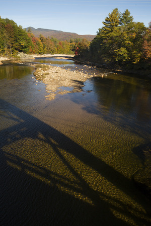 Pemigewasset River in North Woodstock, New Hampshire, in the White Mountains National Forest, with shadows of a bridge and early fall foliage.の写真素材