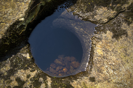 Glacial pothole, filled with water, in bedrock of the Sugar River in Newport, New Hampshire, with some modern grinding rocks inside.の写真素材