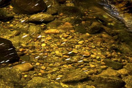 Gentle flow of the Sugar River in Newport, New Hampshire, with colorful underwater rocks and small, silky streaks of foam.の写真素材