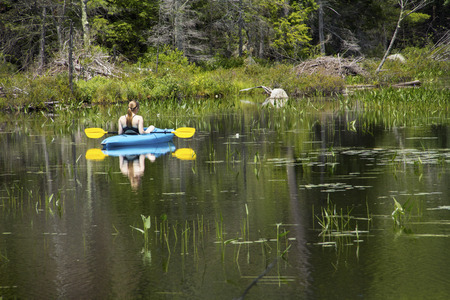 Young woman in blue kayak, coasting right in middle distance on Mud Pond in Sunapee, New Hampshire, on a sunny day, horizontal image.の写真素材