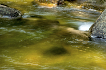 Gentle flow of the Sugar River in Newport, New Hampshire, with colorful underwater rocks and a deep pool.の写真素材