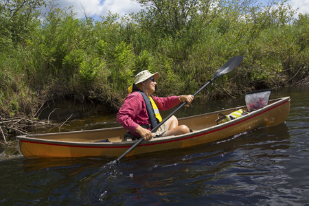 Senior man in an outdoor activity, paddling a small canoe with a kayak paddle on the Moose River near Old Forge, New York, in the Adirondack Mountains.の写真素材
