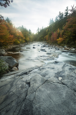 Fall foliage and rapids, with large rock in foreground, at Rocky Gorge of the Swift River in the White Mountains National Forest in northern New Hampshire.の写真素材