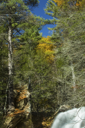 Forest and blue sky at top of Campbell Falls in Norfolk, Connecticut, with some blurred water, fall foliage and granite cliffs.の写真素材