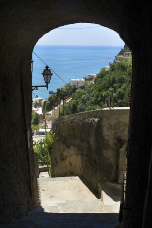 An arch of the pedestrian walkway make a window onto the steep slopes of Positano, Campania, Italy, along the Amalfi Coast. The Mediterranean Sea is in the background.の写真素材