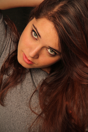 Portrait of attractive young woman with penetrating eyes and an icy glare, head tilted down while looking up, hand behind head.の写真素材