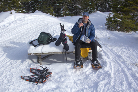 Man on snowshoes resting with a snack at the summit of Bald Mountain in Rangeley, Maine.の写真素材