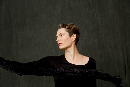 Attractive young woman dancer with short hair, in a scoop neck black dress, swinging a fuzzy black...