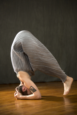 Young woman in silver bag dress beginning a yoga headstand with feet barely off the wood floor of the studio.の写真素材