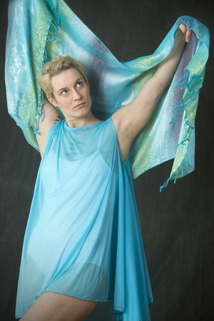 Closeup of young woman dancer with short blonde hair, in a white leotard and blue cape spreading a blue scarf behind her head.の写真素材