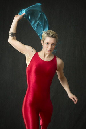 Active young woman dancer with short blonde hair, in a red unitard throwing a blue scarf in the studio.の写真素材