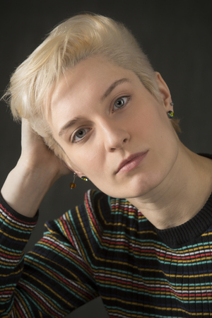 Serious head and shoulders portrait of young blonde woman in colorful striped shirt looking directly into camera.の写真素材
