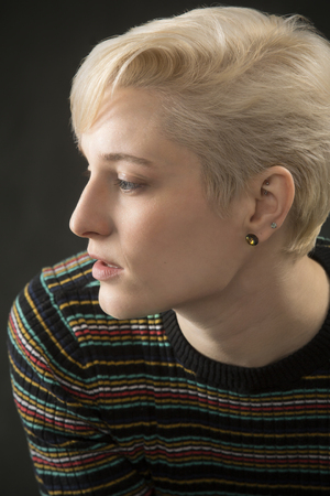 Serious head and shoulders portrait of young blonde woman in colorful striped shirt looking aside.の写真素材