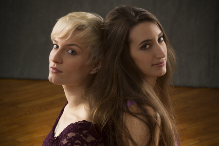 Two young women in purple dresses sitting back to back in the studio, looking calm and beautiful.