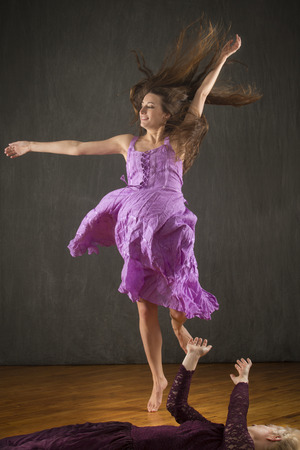 Two young women in purple dresses dancing with enthusiasm on a hardwood floor in the studio.の写真素材