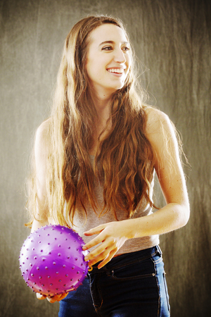 Sunny, high contrast image of attractive young woman with long brown hair playing with a purple ball in an orange glow.の写真素材