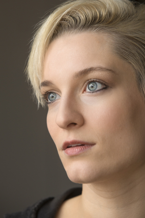 Head and shoulders portrait of  beautiful young woman with short blonde hair looking aside in window light.の写真素材