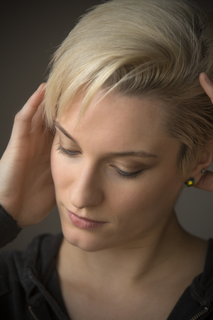 Head and shoulders portrait of  beautiful young woman with short blonde hair, in window light looking down.の写真素材