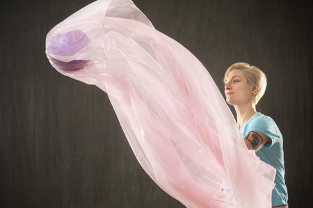 Young woman in casual clothes having fun throwing fabric with a purple ball inside, making it float in the studio.の写真素材