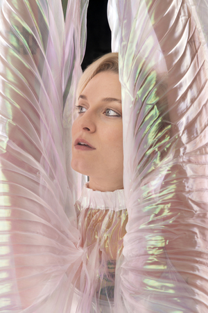 Head and shoulders portrait of a beautiful young woman wrapped in a shimmering transparent cape in the studio.の写真素材