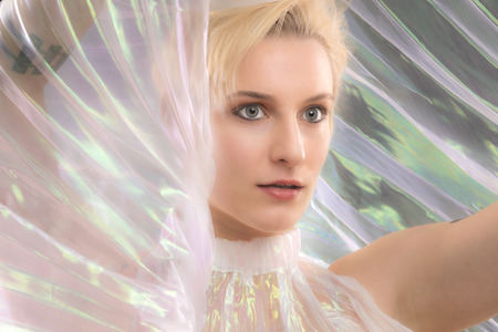 Head and shoulders portrait of a beautiful young woman wrapped in a shimmering transparent cape in the studio.の写真素材