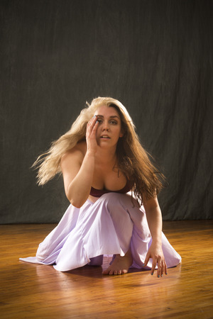 Studio shot of beautiful young dancer in burgundy top and lavender skirt, crouching and leaning forward while dancing in the studio.の写真素材