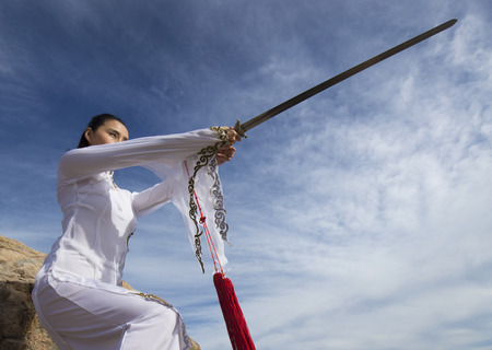 Young woman dancer in white gi performing qi gong with a sword on the rocky beach of Hammonasset State Park in Madison, Connecticut.の写真素材