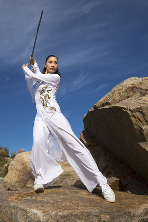 Young woman dancer in white gi performing qi gong with a sword on the rocky beach of Hammonasset State Park in Madison, Connecticut.の写真素材