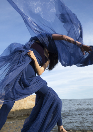 Graceful woman dancer in blue leotard and tights, hurling huge blue fabric into the wind on the beach at Hammonasset State Park in Madison, Connecticut.の写真素材